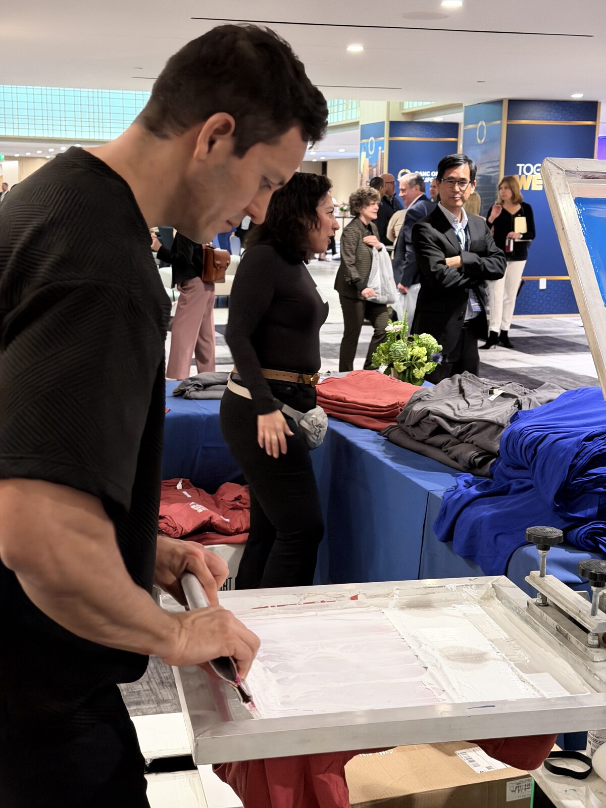 Merch Troop operator working a live station while guests browse folded shirts at a hotel event